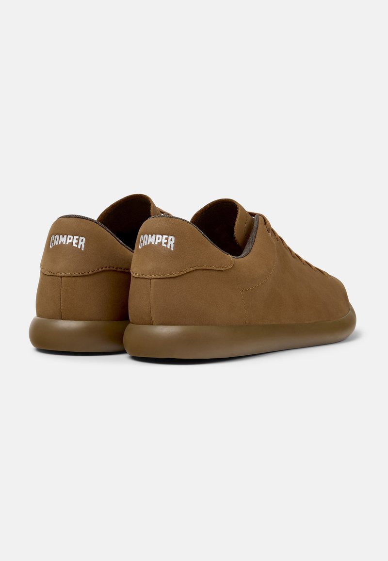 Bruna mockaskor med en slät yta, rundad form och låg profil. Har framträdande vit "Camper"-logotyp på hälen.