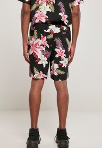 Shorts fleuris avec un fond noir ornés de grandes fleurs de lys roses et blanches, des détails de fougères et une taille élastique.