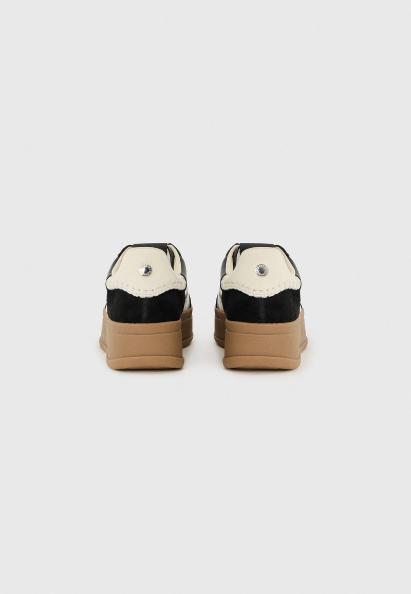 Czarno-kremowe sneakersy z teksturowanym wierzchem, lekko podniesioną podeszwą i dekoracyjnym ściegiem wzdłuż pięty. Szczegół z akcentem w postaci kamienia na tyle.