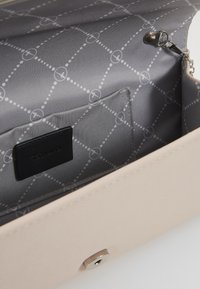 Interno di una borsa in similpelle beige con rivestimento grigio che presenta un motivo geometrico, chiusura a pressione in metallo e una piccola tasca.