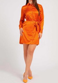 Vestito chemisier arancione con pois, maniche lunghe, colletto, bottoni frontali e cintura in tessuto coordinato. Tessuto liscio e lucido.