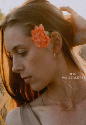 Goldfarbene zarte Halsketten, die auf einem nackten Hals geschichtet sind, mit einer großen orangefarbenen Blume, die das Haar neben dem Ohr betont, vor einem sanften Hintergrund.