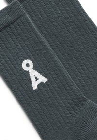 Grijze ribgebreide sokken met een versterkte boord, voorzien van een wit logo-design. Zachte textuur met een gemiddelde dikte.