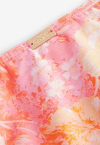 Tkanina s cvetličnim vzorcem v odtenkih roza in oranžne, z zlatim kovinskim oznako s cvetličnim dizajnom. Gladka tekstura, lahka material.