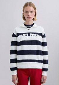 Sudadera de rayas blancas y azul marino con cuello de media cremallera, con el logo "SCALPERS" en blanco en el pecho. Pantalones rojos completan el conjunto.