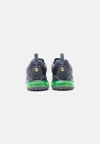 Ζευγάρι γκρι αθλητικά παπούτσια Nike Air Max, εμφανιζόμενα από πίσω, με πράσινες σόλες με αερόσολες και θηλιές στο πίσω μέρος, σε λευκό φόντο.