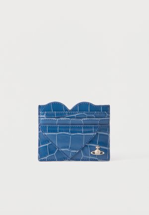 Tarjetero de cuero azul con textura de cocodrilo, detalle en forma de corazón y pequeño emblema plateado de planeta en el frente.