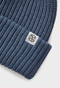 Donkerblauwe gebreide beanie met een gestructureerd ribpatroon en een omgeslagen boord. Bevat een klein wit stoffen label met een zwart logo.