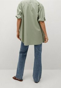 Chemise oversized vert clair avec des manches repliées, ourlet arrondi, assortie à un jean bleu évasé et des sandales marron. Design simple et décontracté.
