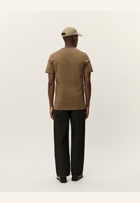 T-shirt court marron en tissu doux, associé à un jean noir ample. Une casquette beige complète la tenue. Texture subtile, coupe décontractée.