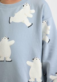Hellblauer Pullover mit weißen Eisbärenmotiven. Die Bären sind in verschiedenen Posen illustriert und haben schwarze Skate-Details. Weicher Stoff.