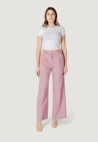 Pantaloni wide-leg rosa chiaro con vita alta, caratterizzati da una chiusura con un solo bottone e pieghe. Abbinati a un top fitted bianco a coste.