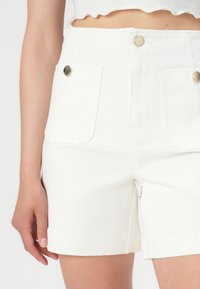 Vita denimshorts med hög midja, två framfickor med guldfärgad knappdetalj, och rak passform med uppvikta fållar.