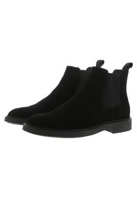 Bottes Chelsea en suede noir avec panneaux latéraux élastiques, bout arrondi et semelle en caoutchouc plate. Équipées de languettes pour un enfilage facile.