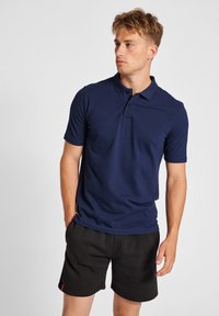 Mörkblå kortärmad polo med krage och treknappsknäppning, tillsammans med svarta sportshorts med en röd detalj. Slät textur.