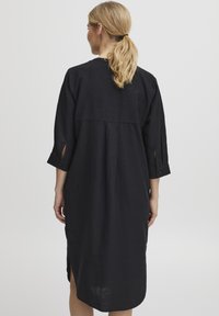 Robe en lin noir à manches trois-quarts, avec des fentes sur les côtés et une coupe décontractée. Design simple et minimal, sans motifs ni embellissements visibles.