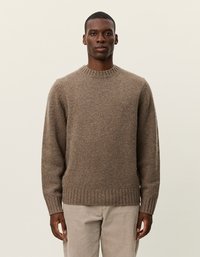 Pull en tricot brun avec col et ourlet côtelés, présentant une coupe légèrement ample et une finition texturée. Porté avec un pantalon de couleur claire.