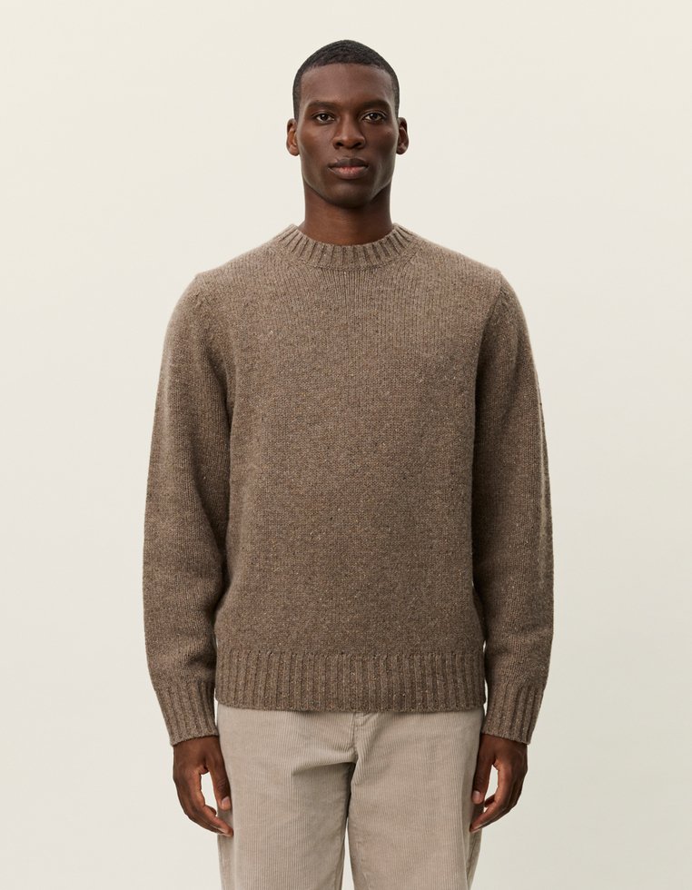 Pull en tricot brun avec col et ourlet côtelés, présentant une coupe légèrement ample et une finition texturée. Porté avec un pantalon de couleur claire.