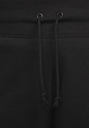 Sorte sweatpants har et ribbet taljebånd med snøreåbninger og tekstureret stof, der fremhæver en glat overflade og ensartet farve.