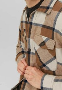 Bruine en crèmekleurige geruite shirt gemaakt van geweven stof, met twee knoopzakken op de borst, donkere knopen en een klassieke kraagontwerp.