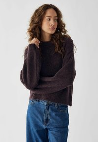 Pulover mov închis cu o croială lejeră, textură moale și mâneci largi, asociat cu blugi din denim albastru cu o croială clasică.