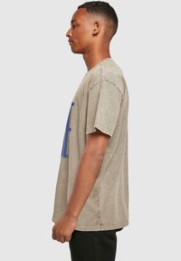 Camiseta oversize color caqui con mangas cortas, que presenta un diseño de texto en azul. Tejido de algodón con una textura suave y un corte relajado.