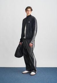 Giacca nera pelosa con strisce bianche, abbinata a pantaloni da tuta neri. Gli accessori includono una borsa nera. Le scarpe bianche aggiungono contrasto.