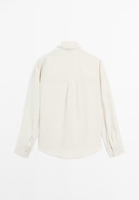 Light beige button-up shirt with long sleeves, a pointed collar, pleat detail at the back, and cuff buttons. Smooth texture, casual design.