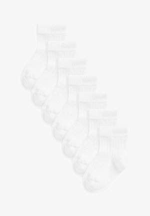 Chaussettes blanches en coton, avec une texture côtelée et des poignets élastiques, disposées en une pile de six paires.