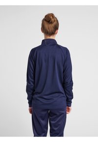 Marinblå långärmad träningströja med hög krage, texturerad tyg och raglanärmar, kombinerad med matchande byxor i slätt material.