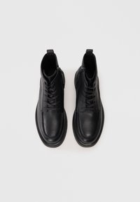 Par de botas de cuero negro hasta el tobillo con cordones y cremalleras laterales, vistas desde arriba sobre un fondo blanco.