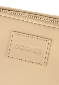 Beżowy materiałowy woreczek z fakturowaną skórzaną metką wytłaczaną napisem "BOGNER". Posiada gładki zamek błyskawiczny i minimalistyczny design.