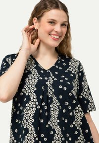 Květinový top s výstřihem do V v námořnické modři, zdobený bílým a modrým květinovým potiskem, s krátkými rukávy a plisovaným detailem vpředu.