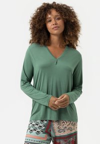 Langarm, V-hals top in groene stof met een gladde textuur. Gecombineerd met gestreepte broek met geometrische ontwerpen en warme kleuren.