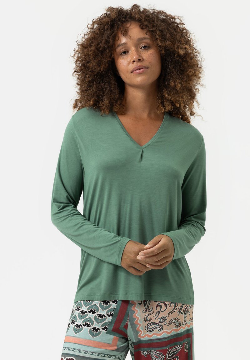 Langarm, V-hals top in groene stof met een gladde textuur. Gecombineerd met gestreepte broek met geometrische ontwerpen en warme kleuren.