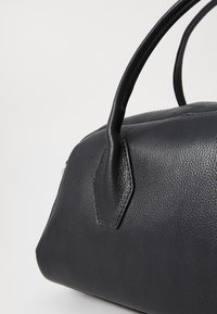 Bolsa de couro preta com superfície texturizada, forma arredondada e duas alças resistentes. Acentuada com um detalhe hexagonal na lateral.