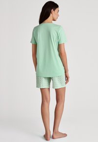Mintgrünes Baumwoll-T-Shirt mit kurzen Ärmeln, kombiniert mit gemusterten mintgrünen Shorts mit geometrischem Design. Geeignet für die Freizeit.