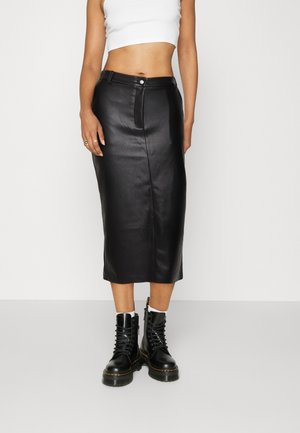 Femme portant une jupe midi en cuir noir taille haute, un top court blanc, des chaussettes blanches et des bottes de combat noires à lacets.
