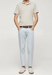 Beige polo tričko, světle modré džíny, hnědý kožený opasek a béžové tenisky s akcenty. Slim fit a ležérní design.