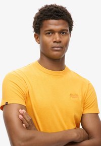 Kortærmet gul bomulds T-shirt med rund hals, der har et lille logo på brystet. Glat tekstur og almindelig pasform.