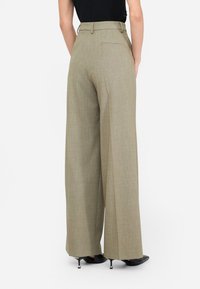 Pantaloni a gamba larga in tessuto khaki chiaro strutturato, con dettagli alle tasche posteriori e vita alta, abbinati a scarpe con tacco nere.