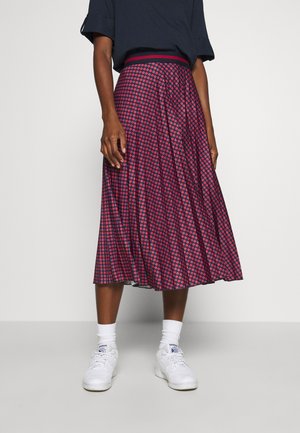 Femme portant un haut bleu marine avec une jupe midi plissée à pois rouges et bleu marine, ainsi que des baskets blanches avec des chaussettes blanches.