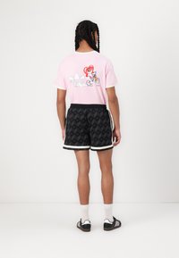 Pink t-shirt with a cartoon graphic on the back, paired with black shorts featuring a geometric pattern and white trim.