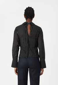 Blusa a maniche lunghe a righe bianche e nere con scollatura posteriore, chiusura a fiocco al collo e maniche a campana. Materiale morbido e leggero.
