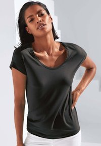 Zwart T-shirt met korte mouwen en een brede ronde halslijn, gecombineerd met witte broek. De stof lijkt lichtgewicht en aansluitend te zijn.