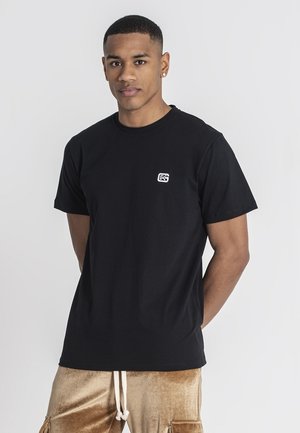 Camiseta de algodón negra con escote redondo y mangas cortas. Presenta un pequeño logotipo blanco en la parte izquierda del pecho. Diseño simple y clásico.