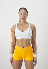 Hvitt sports-BH med logo, sammen med lys gule kompresjonsshorts med logo på livet. Glatt stoff, tettsittende design.