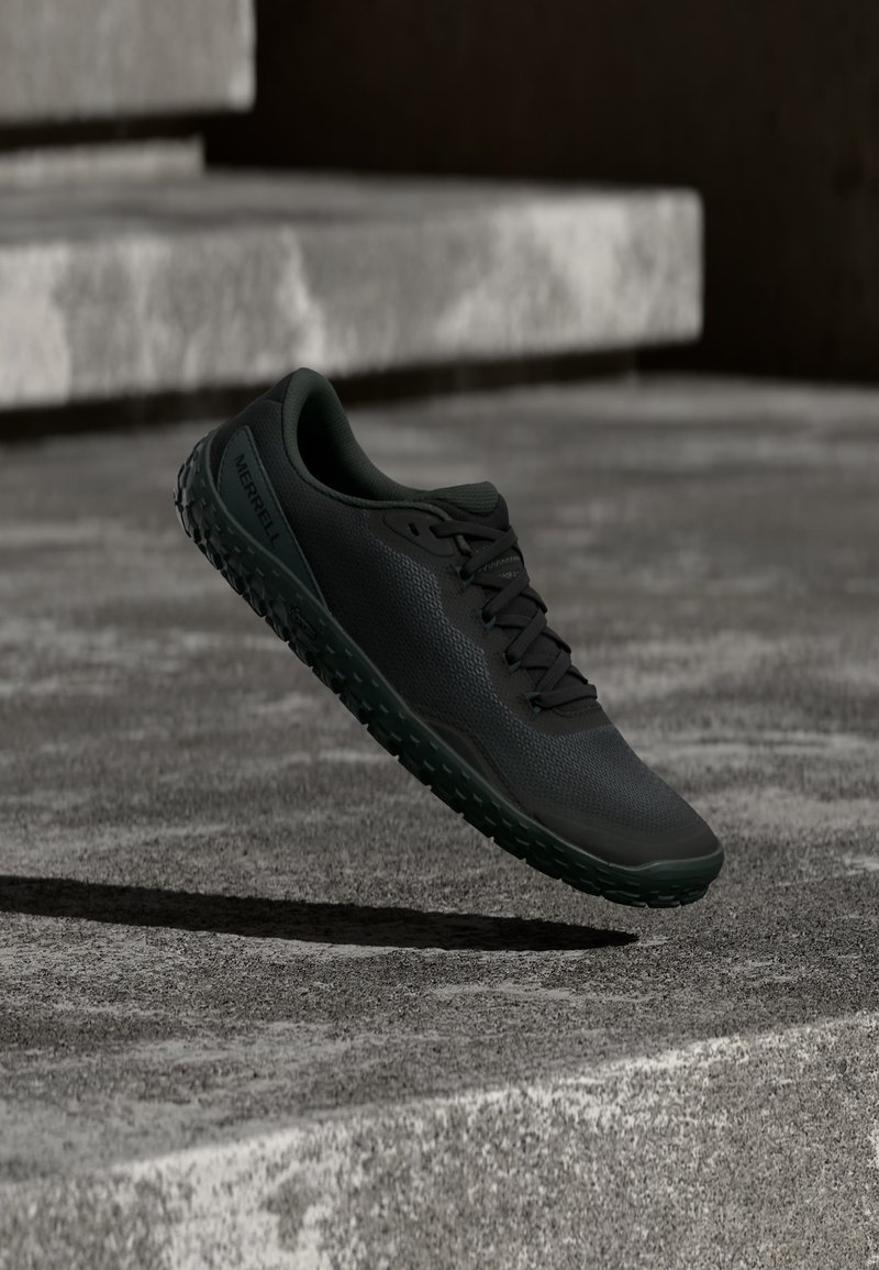 Μαύρο ορειβατικό παπούτσι με υφασμένη σόλα αιωρούμενο πάνω από τσιμεντένια σκαλοπάτια σε σκηνικό με χαμηλό φωτισμό.