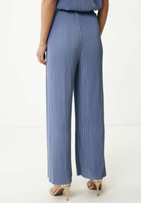 Jasnoniebieskie, szerokie spodnie z plisowanej tkaniny; elastyczny pas i gładka faktura. Noszone z cielistymi butami na wysokim obcasie.