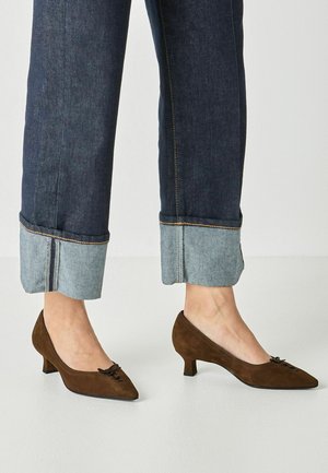 Ben iført mørke opsmøgede jeans og brune ruskind kitten heel sko med spidse tæer og lille sløjfedetalje.